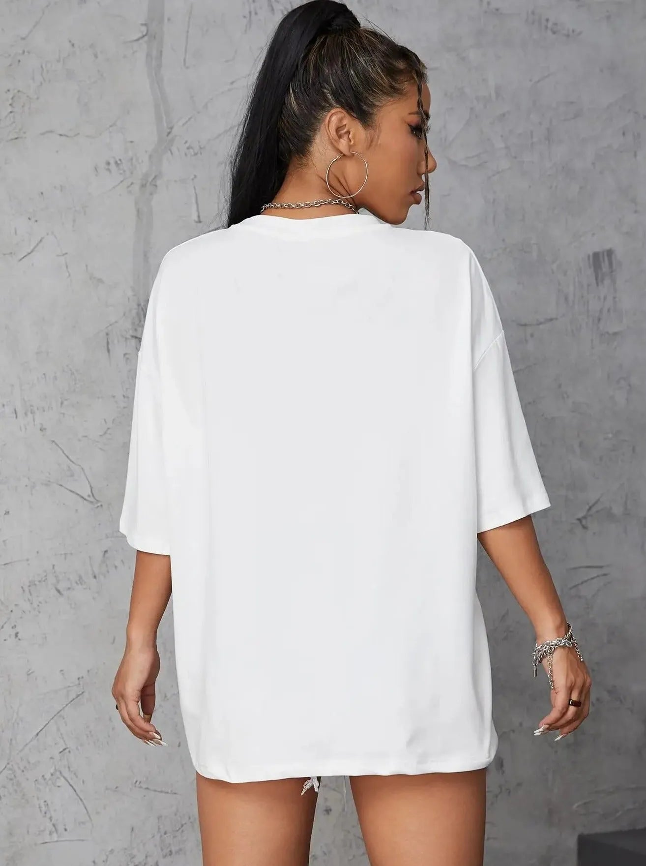 Frau in weißem Oversize-T-Shirt, Rückansicht, vor grauer Wand. Modetrend, lässiger Stil, Streetwear, Damenmode, minimalistisch.