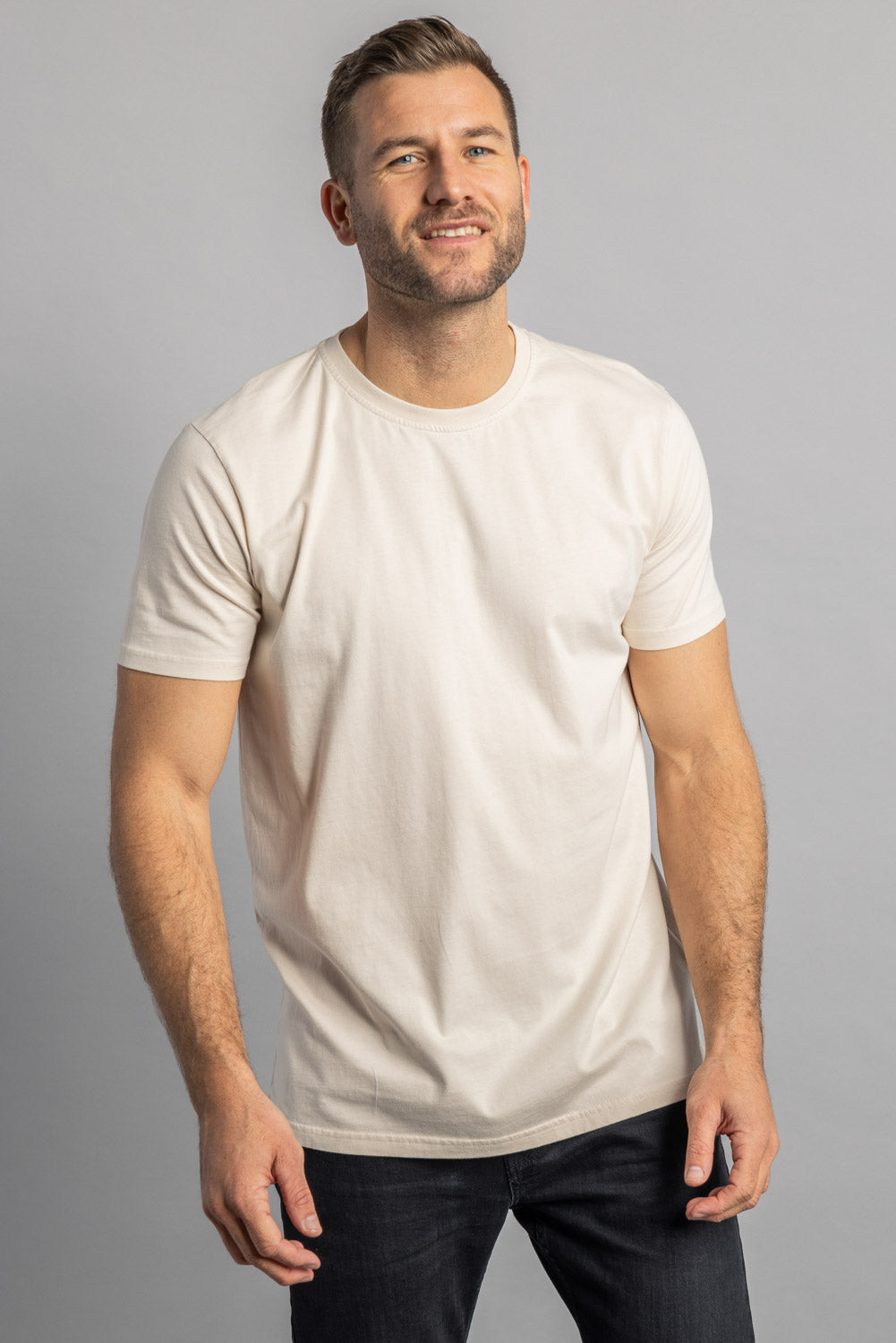 Mann in weißem T-Shirt, lächelnd, vor grauem Hintergrund, Mode, Freizeitkleidung.
