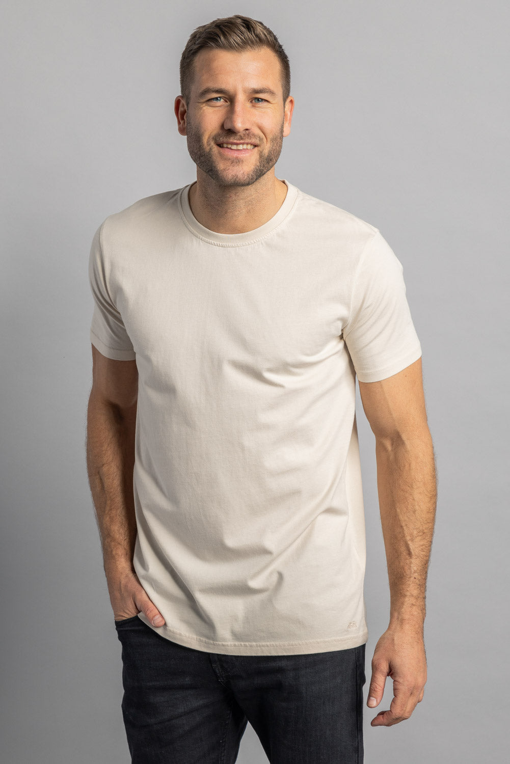 Mann in cremefarbenem T-Shirt, lächelnd, vor grauem Hintergrund, Mode, Herrenbekleidung.