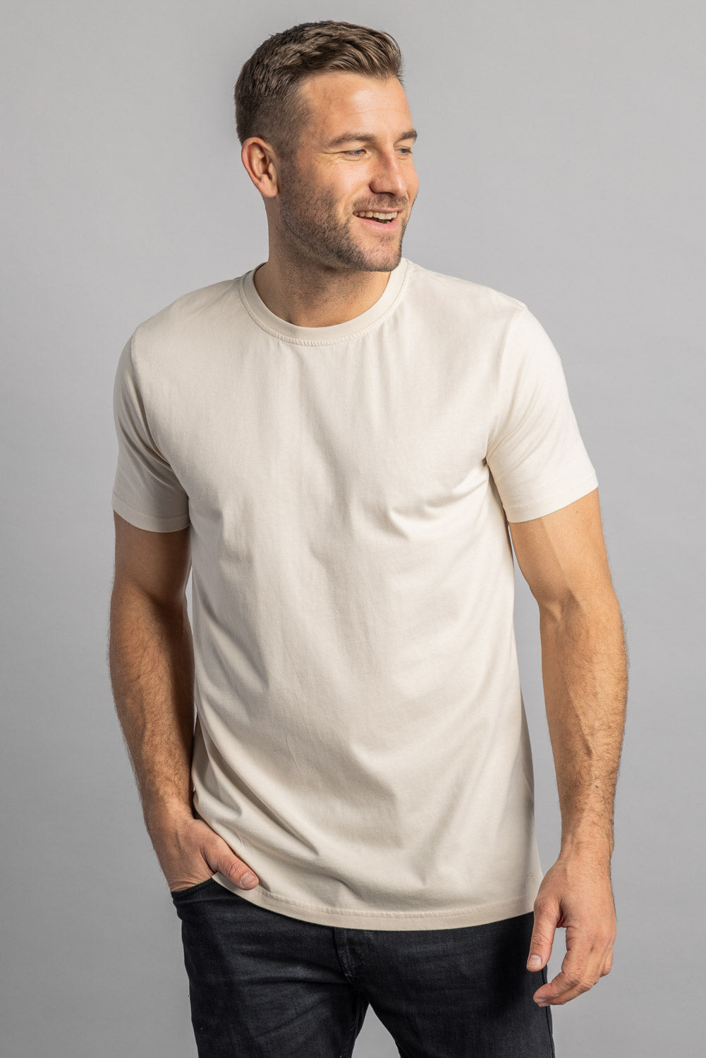 Mann trägt cremefarbenes T-Shirt, lächelt, grauer Hintergrund, Mode, Herrenbekleidung.