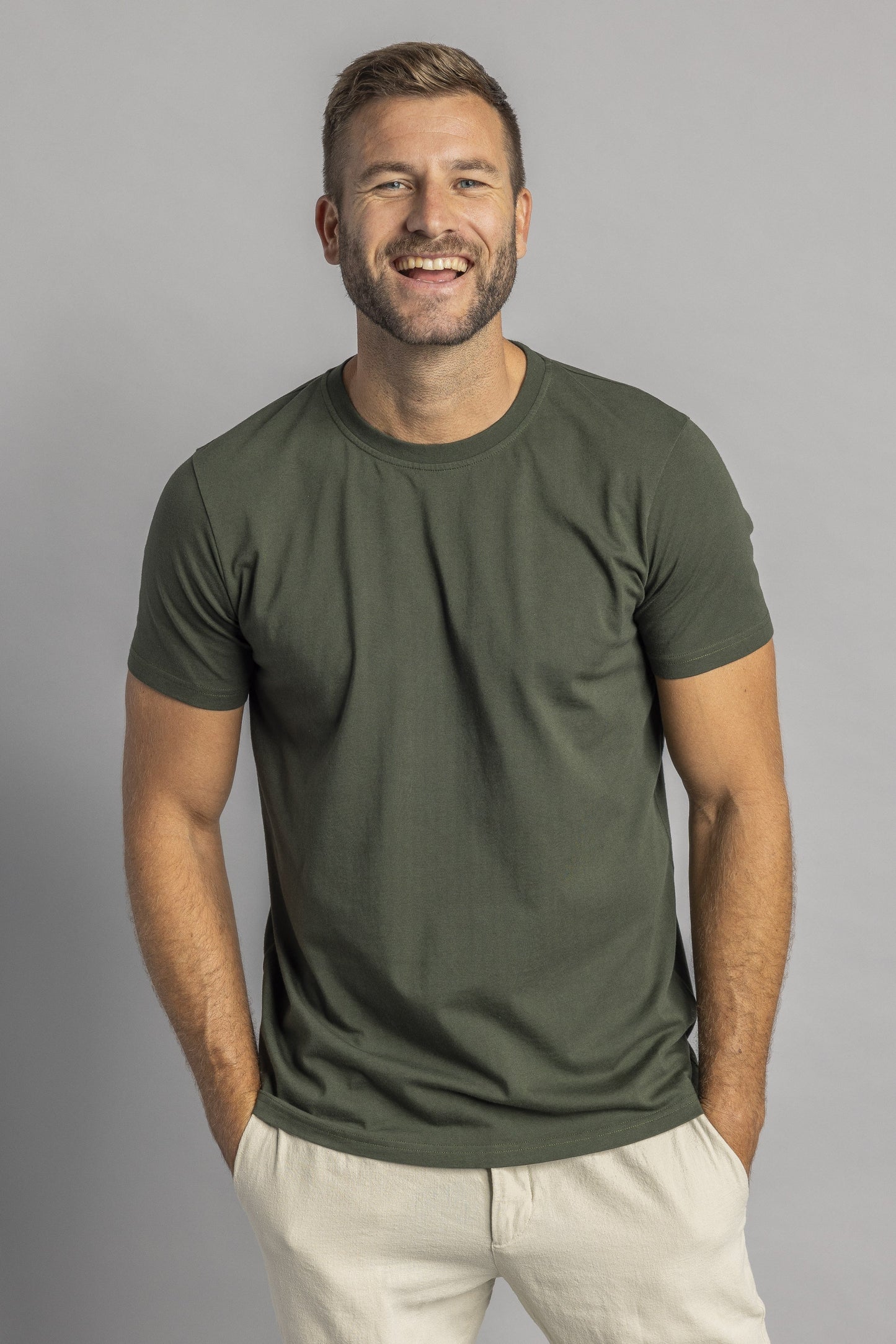 Mann in olivgrünem T-Shirt, lächelnd, vor grauem Hintergrund, Freizeitmode Herren.