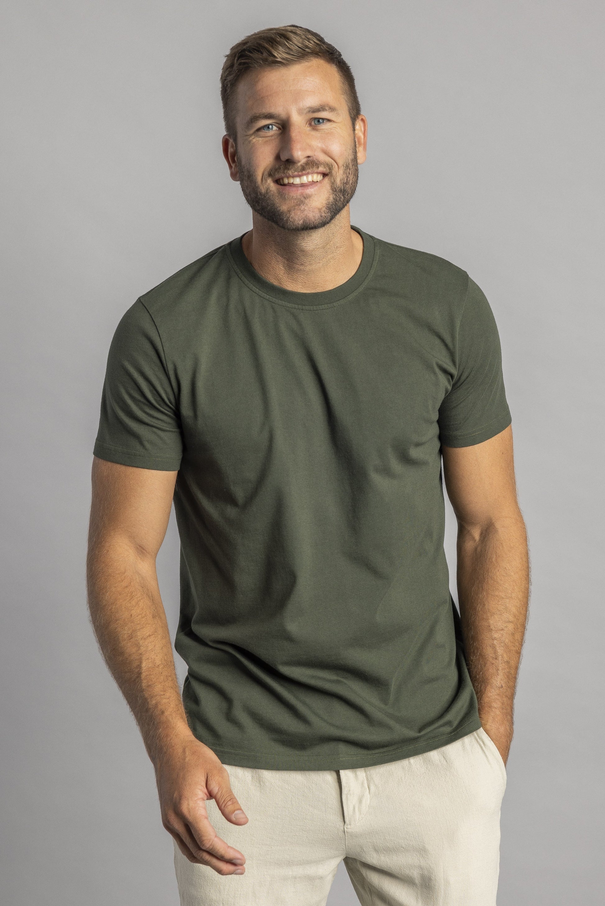 Mann in olivgrünem T-Shirt, lächelnd, vor grauem Hintergrund, lässige Mode, Herrenbekleidung.