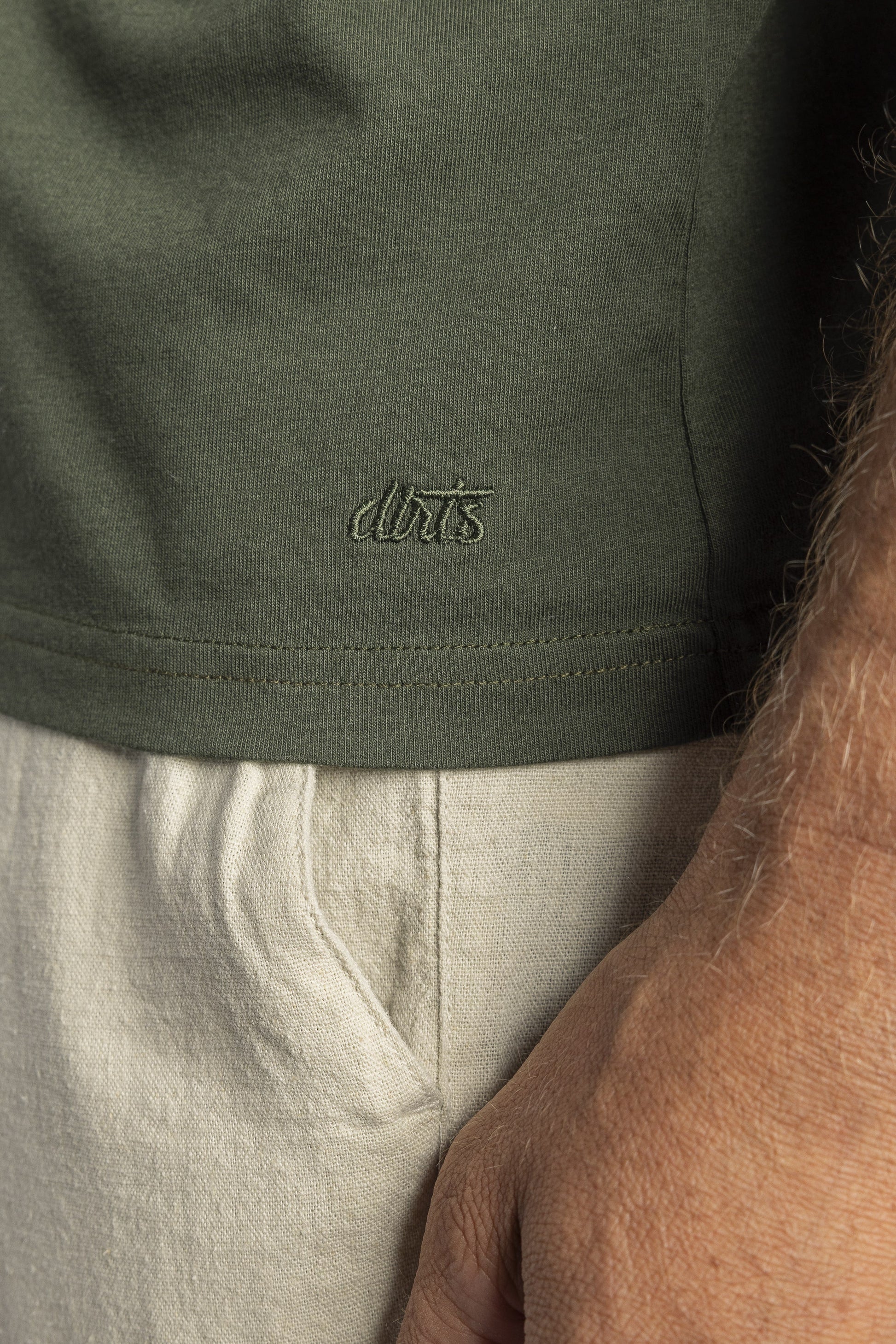 Grünes T-Shirt aus Baumwolle mit Logo-Stickerei, kombiniert mit beiger Hose, Nahaufnahme.
