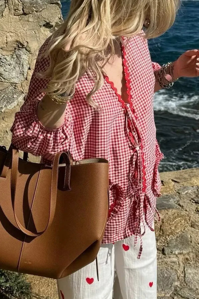 Frau in kariertem Hemd und weißer Hose mit Herzen, hält braune Ledertasche. Sommermode, Strand, lässiger Stil, Damenbekleidung.