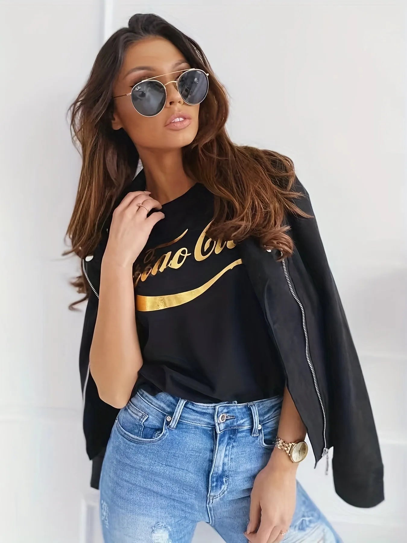 Frau in modischer Sonnenbrille, schwarzem T-Shirt und Jeans, lässig mit Jacke über der Schulter. Trendige Damenmode, Streetstyle, Accessoires.