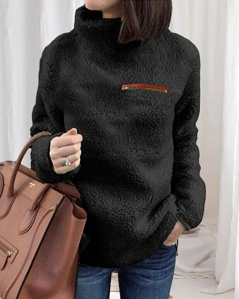 Damen Teddy-Fleece-Pullover in Schwarz mit hohem Kragen und Reißverschlusstasche, kombiniert mit brauner Handtasche und blauer Jeans.