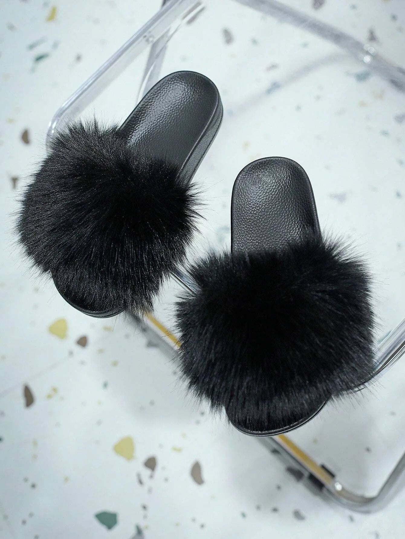 Schwarze Pelzhausschuhe auf transparentem Stuhl, luxuriöses Design, gemütliche Damenmode, stilvolle flauschige Pantoffeln für Zuhause.