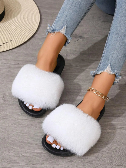 Weiße flauschige Hausschuhe auf Holzfußboden, getragen mit zerrissenen Jeans. Modische Damen-Slipper, bequem und stilvoll für den Alltag.