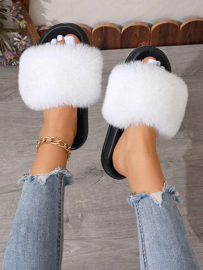 Weiße flauschige Hausschuhe auf grauem Holzboden, getragen von Person in zerrissenen Jeans. Modische Damen-Slipper, bequem und stilvoll.