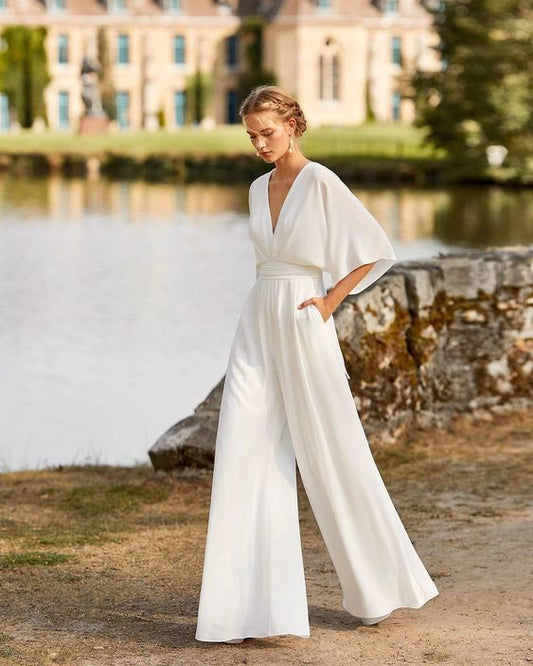 Eleganter weißer Jumpsuit mit tiefem V-Ausschnitt und weiten Ärmeln, ideal für Hochzeiten oder formelle Anlässe, vor malerischer Schlosskulisse.