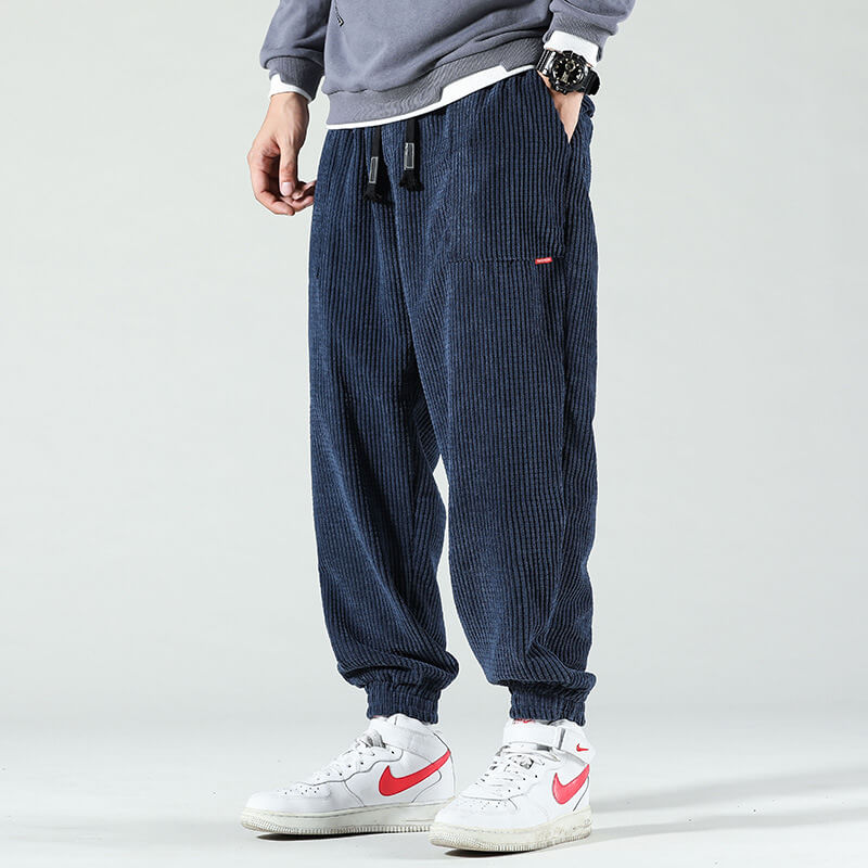 Mann trägt blaue Cordhose, grauen Pullover, weiße Nike-Sneaker, lässiger Streetwear-Look.