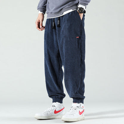 Mann trägt blaue Cordhose, grauen Pullover, weiße Nike-Sneaker, lässiger Streetwear-Look.