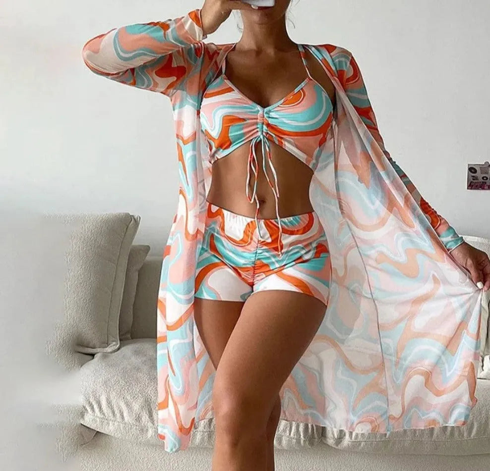 Frau in buntem, gemustertem Strandoutfit mit Crop-Top, Shorts und Kimono. Sommermode, Strandkleidung, trendige Damenbekleidung.