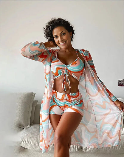 Frau in buntem, gemustertem Strandoutfit mit Kimono und Shorts, lächelnd im Wohnzimmer. Sommermode, Damenbekleidung, Freizeitlook.
