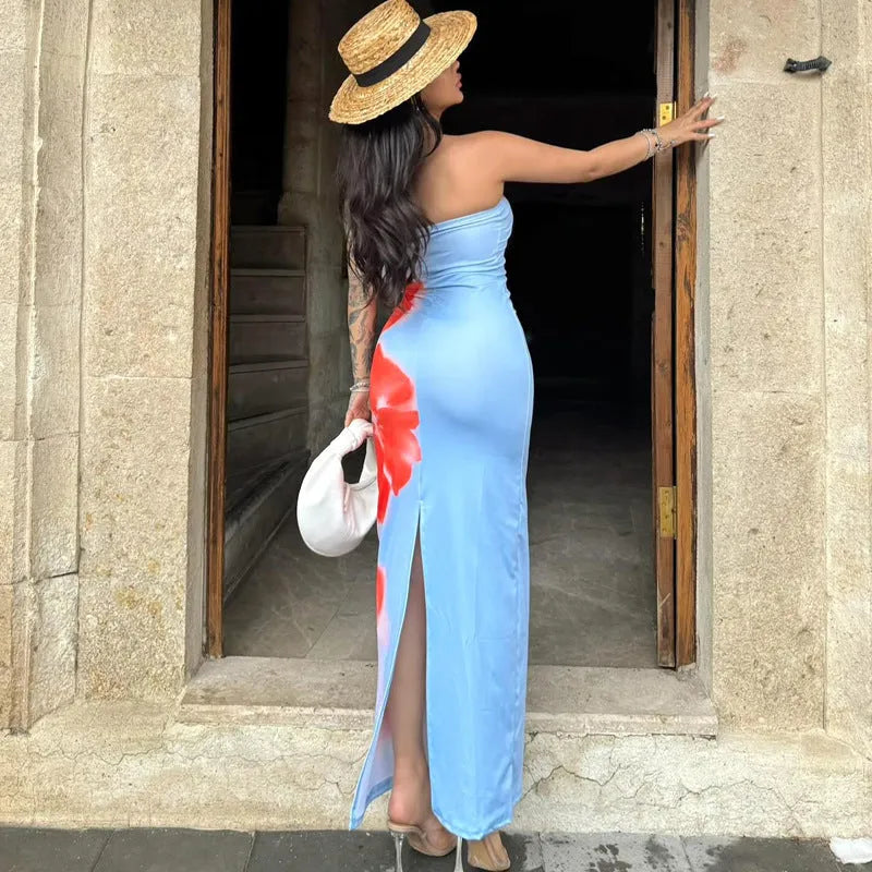 Frau in blauem Kleid mit rotem Blumenmuster und Strohhut, steht in Türrahmen. Sommermode, elegantes Abendkleid, modische Accessoires.