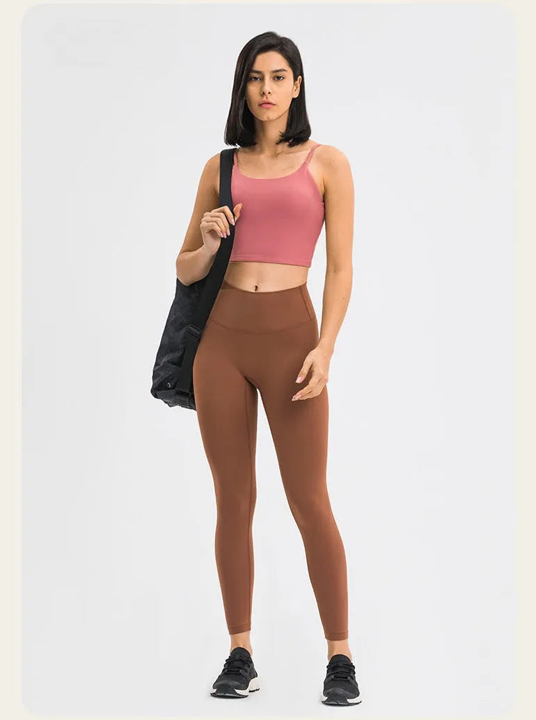 Frau in sportlicher Kleidung: rosa Sport-BH, braune Leggings, schwarze Sneakers, schwarze Tasche. Fitnessmode, Damenbekleidung, Sportoutfit.