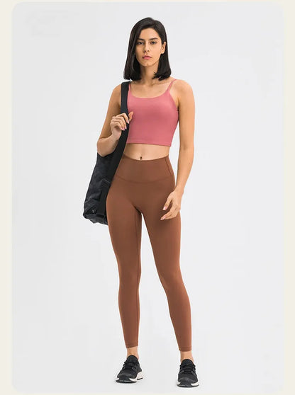 Frau in sportlicher Kleidung: rosa Sport-BH, braune Leggings, schwarze Sneakers, schwarze Tasche. Fitnessmode, Damenbekleidung, Sportoutfit.
