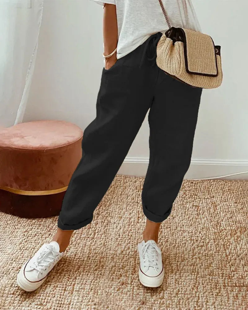 Damenmode: Lässige schwarze Jogginghose, kombiniert mit weißen Sneakers und beiger Umhängetasche. Perfekt für Freizeit und Streetstyle.