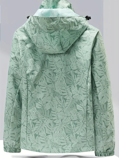 Damenjacke mit Kapuze, grün, mit tropischem Blattmuster. Wasserabweisend, ideal für Outdoor-Aktivitäten. Modisch und funktional.