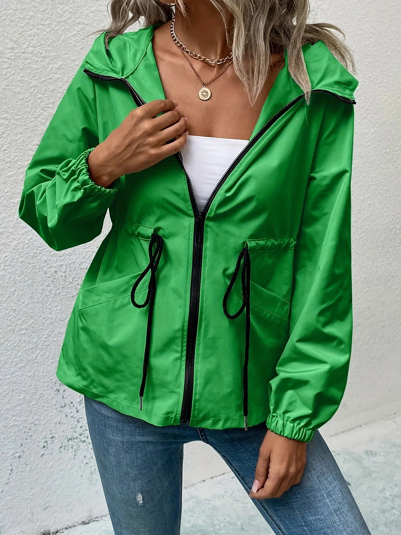 Grüne Damenjacke mit Kapuze, Reißverschluss und Kordelzug, kombiniert mit blauer Jeans. Modische Freizeitkleidung für den Herbst.