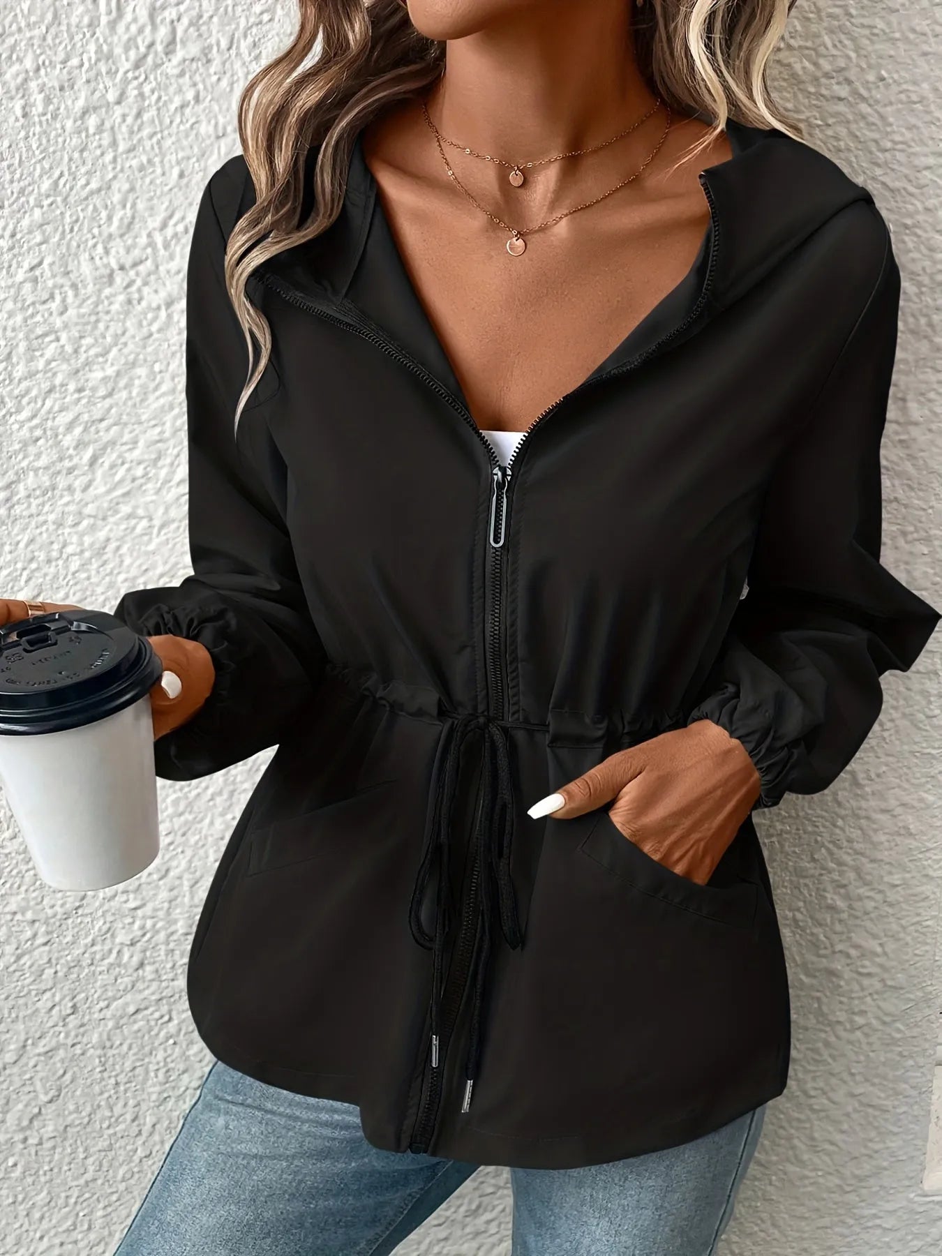 Damenjacke mit Reißverschluss, Kapuze und Kordelzug in Schwarz. Perfekt für Freizeitmode. Kombiniert mit Jeans und Kaffeebecher.