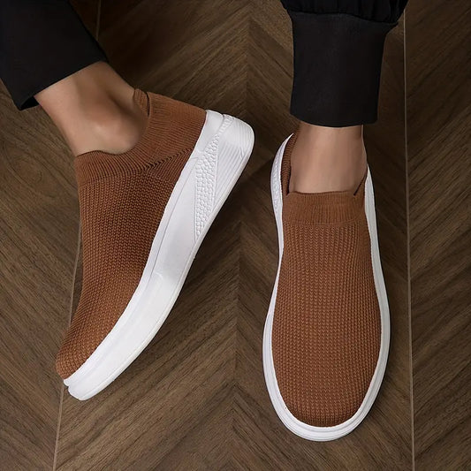 Braune Slip-On-Sneaker mit weißer Sohle auf Holzfußboden. Bequeme, modische Freizeitschuhe für Herren. Ideal für Alltag und Freizeit.