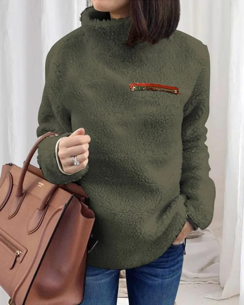 Damenmode: Grüner Teddyfleece-Pullover mit hohem Kragen und Reißverschluss-Detail, kombiniert mit brauner Lederhandtasche. Wintermode, gemütlich, stilvoll.