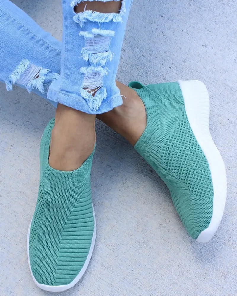Grüne Slip-On-Sneaker mit gestricktem Obermaterial und weißer Sohle, kombiniert mit zerrissenen Jeans. Bequeme, modische Freizeitschuhe.