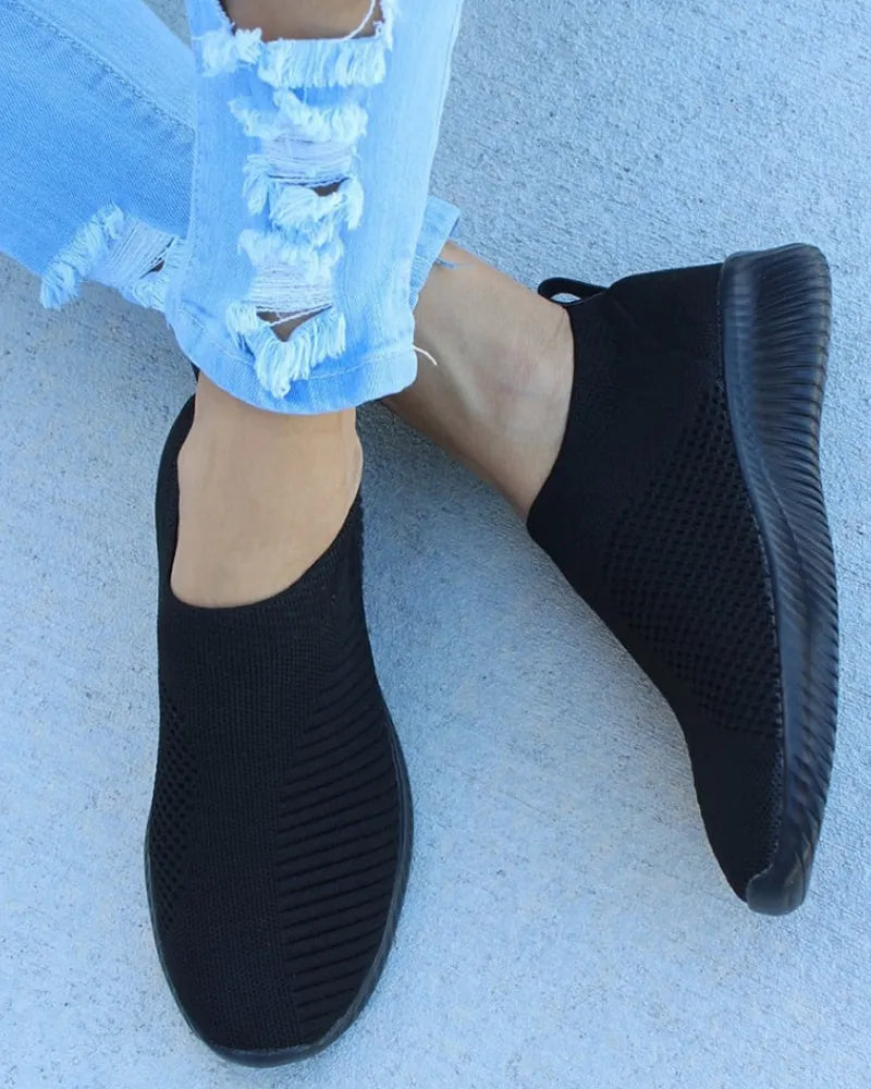 Schwarze Sneaker aus atmungsaktivem Strickmaterial, kombiniert mit zerrissenen Jeans. Bequeme, modische Schuhe für Damen, ideal für Freizeit und Alltag.