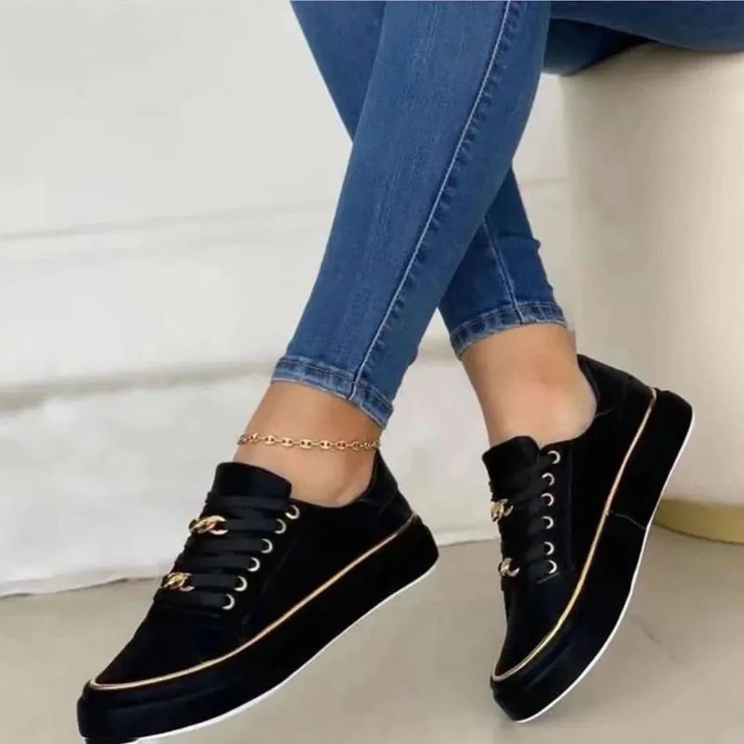 Schwarze Damen-Sneaker mit goldenen Details, kombiniert mit blauen Jeans. Modische, bequeme Schuhe für Alltag und Freizeit.