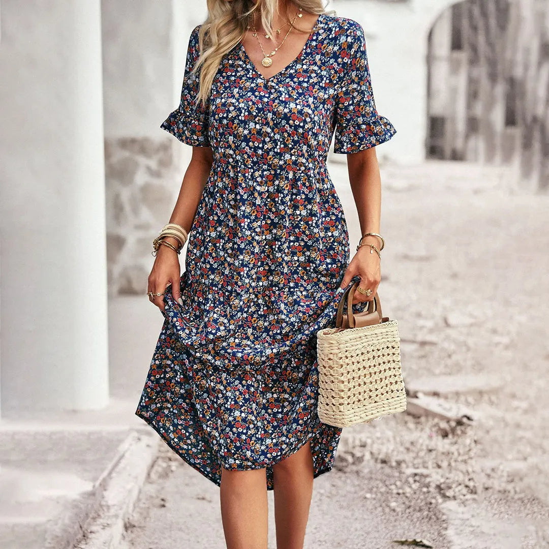 Frau in geblümtem Sommerkleid mit V-Ausschnitt und Rüschenärmeln, hält eine geflochtene Strohtasche. Perfekt für lässige Sommermode.