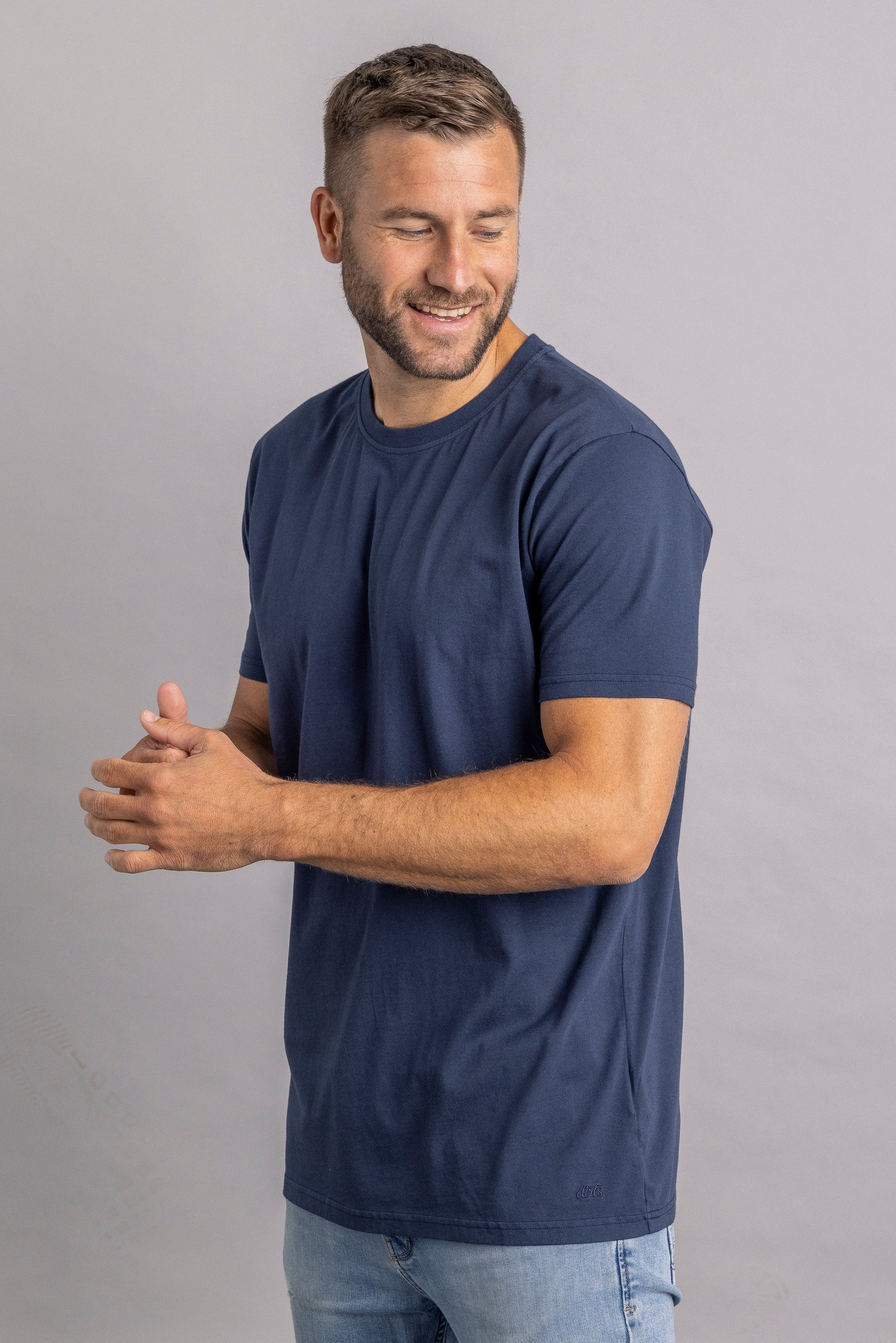Mann in dunkelblauem T-Shirt, lächelnd, grauer Hintergrund, Freizeitmode, Herrenbekleidung.
