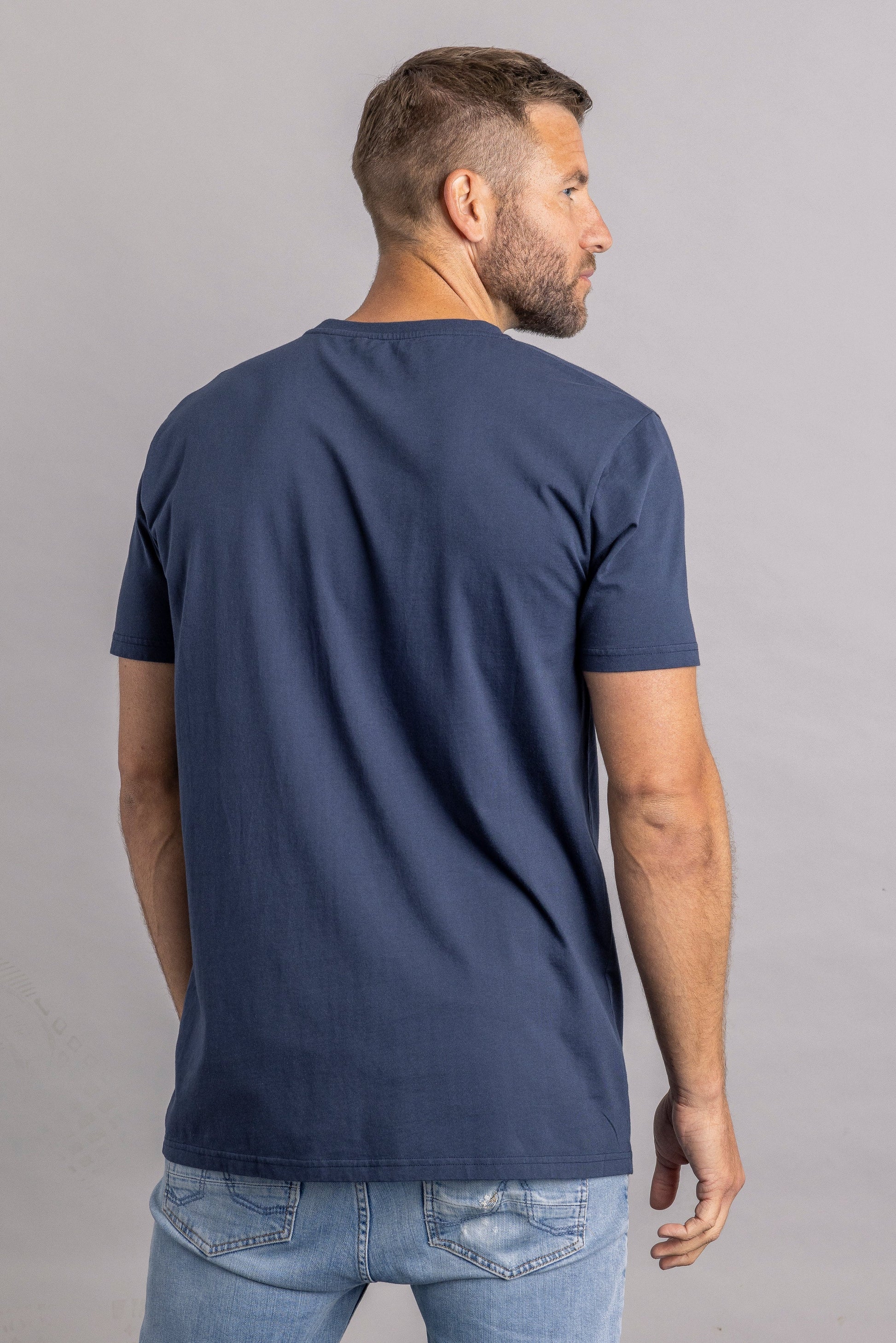 Mann in dunkelblauem T-Shirt und Jeans, Rückansicht, lässige Herrenmode, Freizeitkleidung.