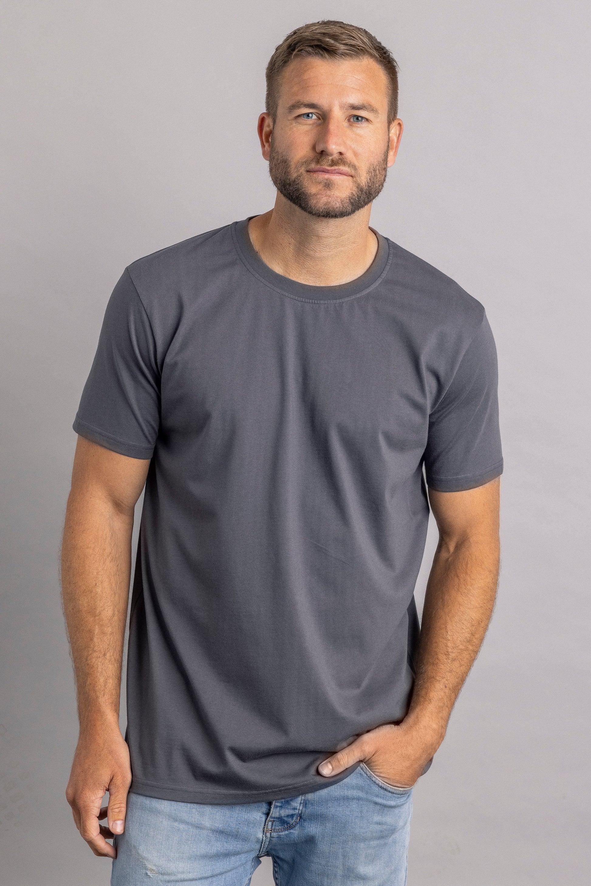 Mann in grauem T-Shirt und blauer Jeans vor grauem Hintergrund.