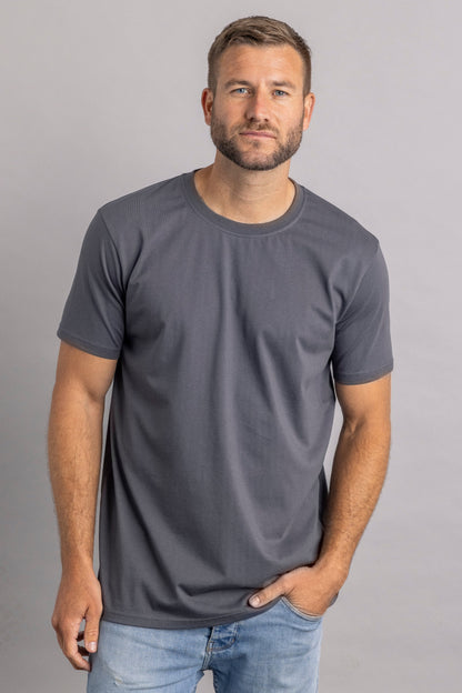 Mann in grauem T-Shirt und blauer Jeans vor grauem Hintergrund.