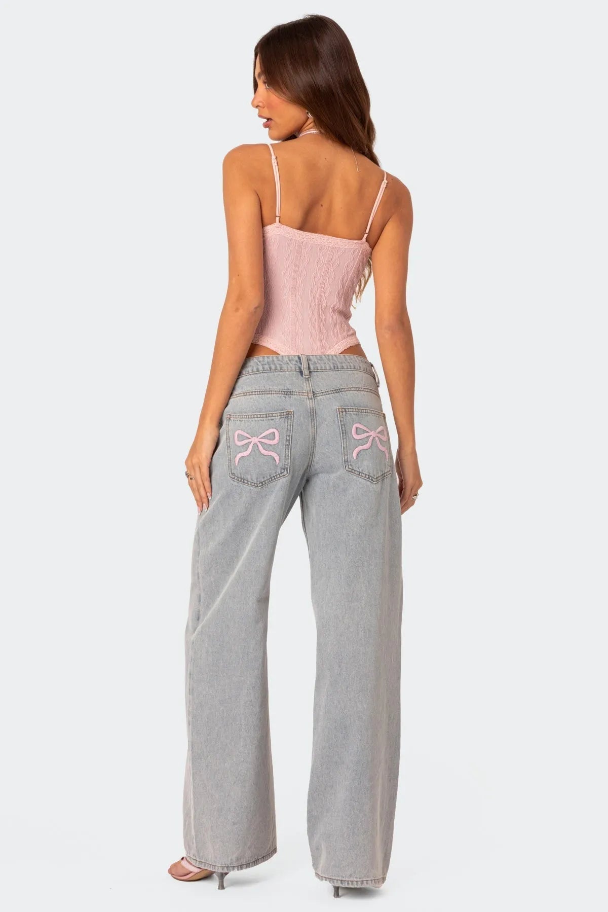 Frau in rosa Top und weiten Jeans mit Schleifen-Details auf den Taschen. Modetrend, Damenbekleidung, lässiger Look, stilvolle Outfits.