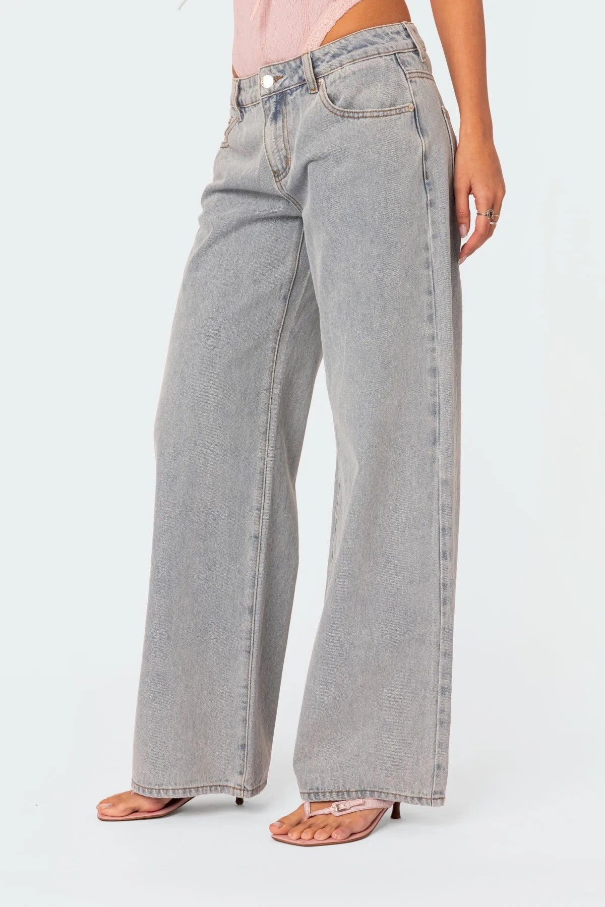Graue, weite Jeans für Damen, kombiniert mit rosa Oberteil und Sandalen. Modetrend, lässiger Stil, ideal für Freizeitoutfits.