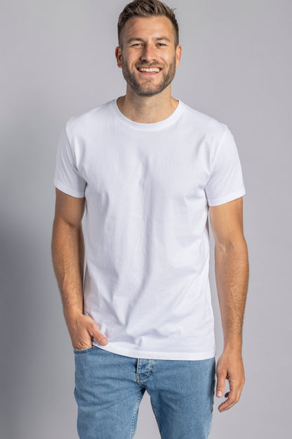 Lächelnder Mann in weißem T-Shirt und blauer Jeans vor grauem Hintergrund.