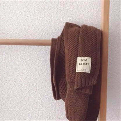 Brauner Strickpullover mit Etikett "MIA Bonbon" auf Holzkleiderbügel, minimalistisch, gemütlich, Herbstmode, hochwertiger Strick, stilvoll.