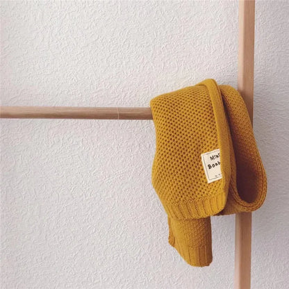 Gelber Strickschal aus Baumwolle, stilvoll drapiert auf Holzstange. Perfekt für Herbstmode, warm und modisch. Ideal für Damen und Herren.