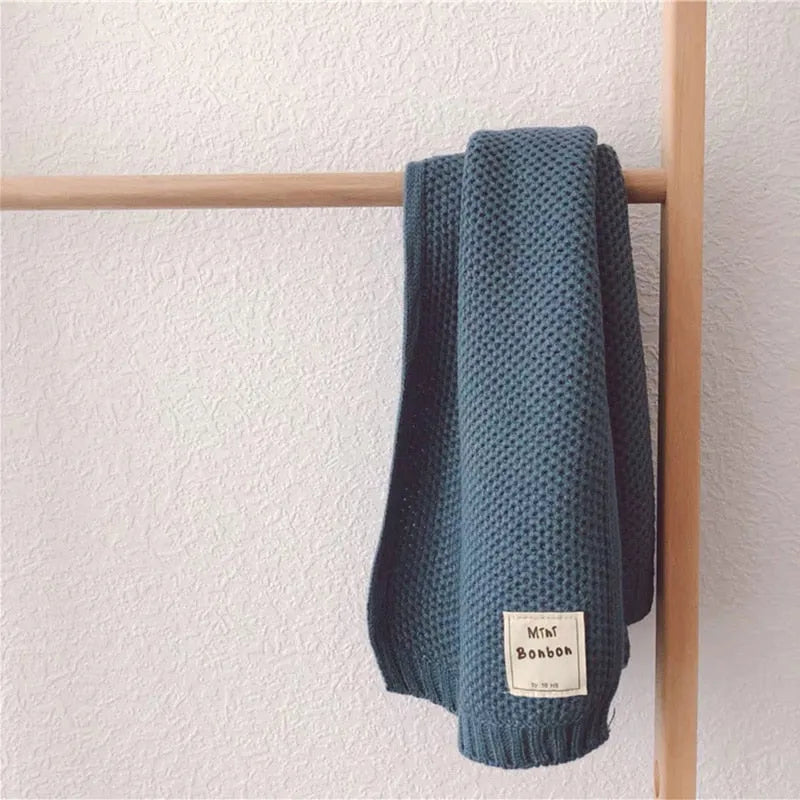 Strickdecke in Blau, gehängt auf Holzstange, mit Etikett "Mini Bonbon". Perfekt für gemütliche Wohnkultur, modernes Design, hochwertige Textilien.