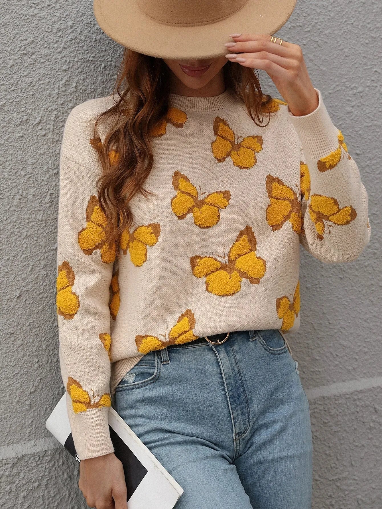 Damenpullover mit gelbem Schmetterlingsmuster, kombiniert mit blauer Jeans und beigem Hut. Modetrend, Herbstmode, Strickpullover.