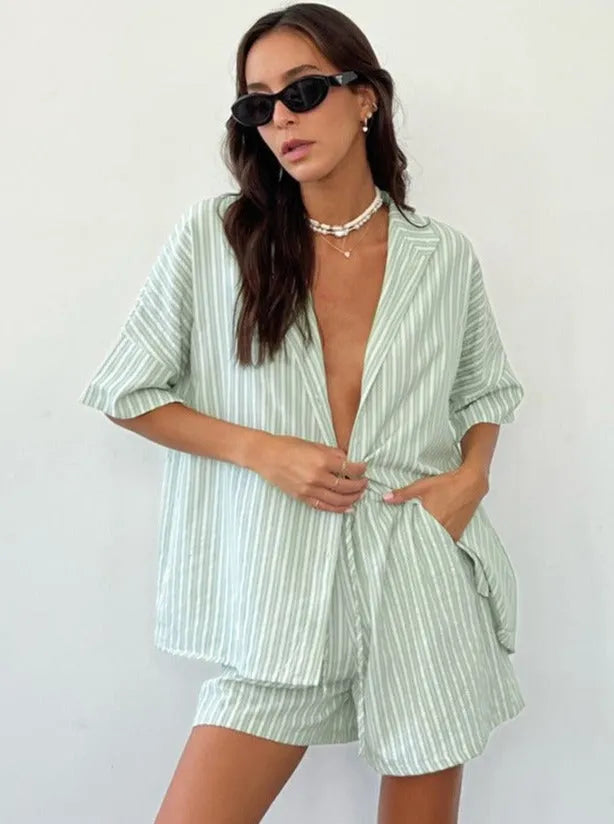 Frau in gestreiftem, mintgrünem Kurzarm-Anzug mit Shorts, Sonnenbrille und Perlenkette. Modetrend, Sommeroutfit, lässiger Stil.