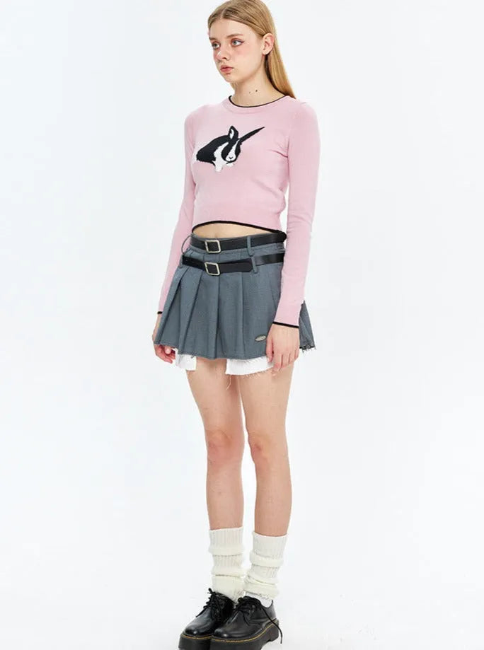 Junge Frau in rosa Langarmshirt mit Pinguin-Design, grauem Faltenrock, weißen Socken und schwarzen Schuhen. Modetrend, Streetwear, Jugendstil.