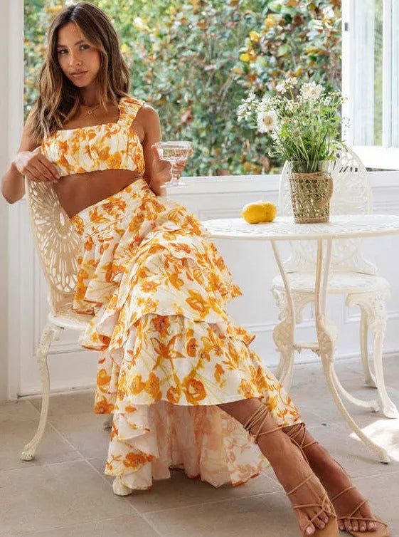 Frau in geblümtem Sommerkleid sitzt elegant an einem weißen Tisch mit Cocktailglas. Perfekt für Mode, Sommerkleider, Damenmode, Freizeitlook.