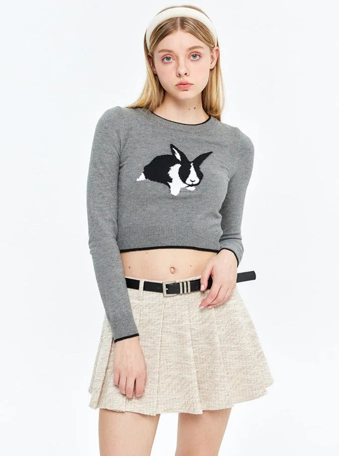 Grauer Pullover mit Hasenmotiv, kombiniert mit beiger Faltenrock. Modetrend, Damenmode, lässiger Look, stilvoller Pullover, Herbstmode.