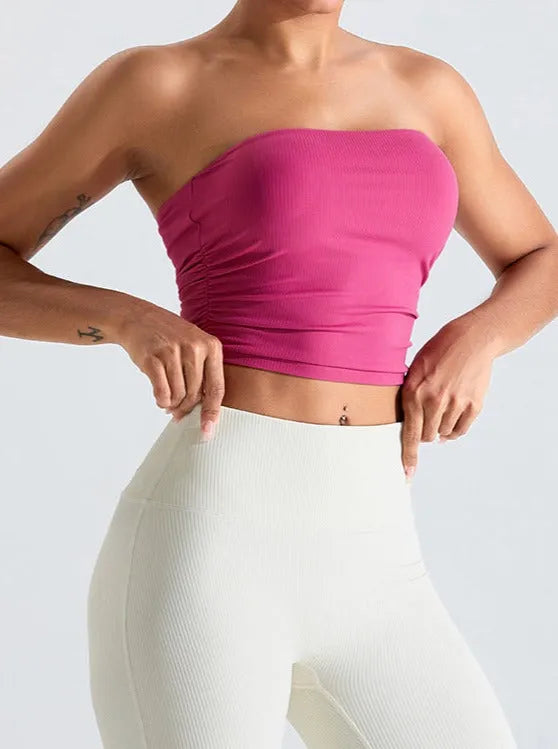 Frau in pinkem Bandeau-Top und weißen Leggings, sportlich, modisch, Fitness-Outfit, bequeme Sportbekleidung, trendige Damenmode.