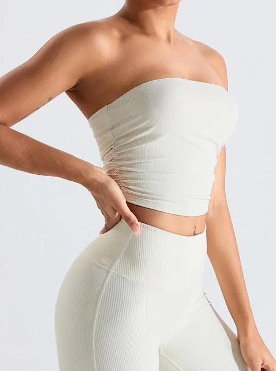Damen in cremefarbenem, schulterfreiem Crop-Top und Leggings. Modische Sportbekleidung, nahtloses Design, ideal für Fitness und Freizeit.