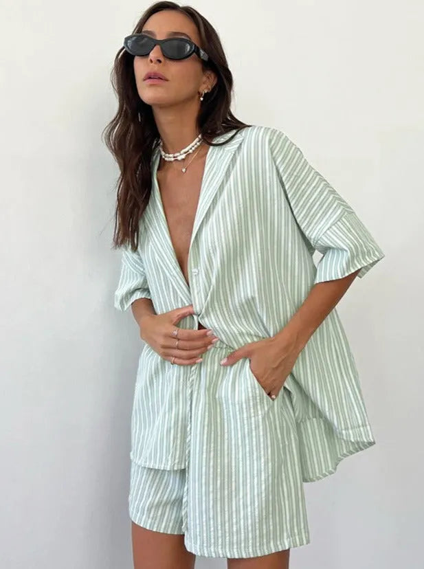 Frau in gestreiftem, grün-weißem Sommer-Set mit Hemd und Shorts, Sonnenbrille und Perlenkette. Modetrend, lässiger Stil, Damenbekleidung.
