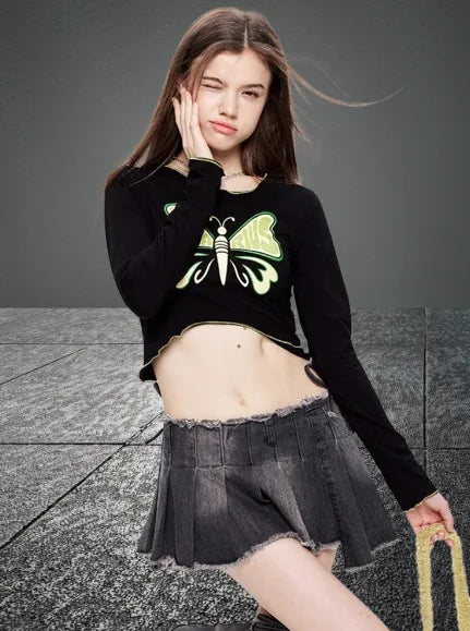 Junge Frau in modischem Outfit: Schwarzes Langarmshirt mit Schmetterlingsmotiv, grauer Faltenrock. Trendige Streetwear für Jugendliche.